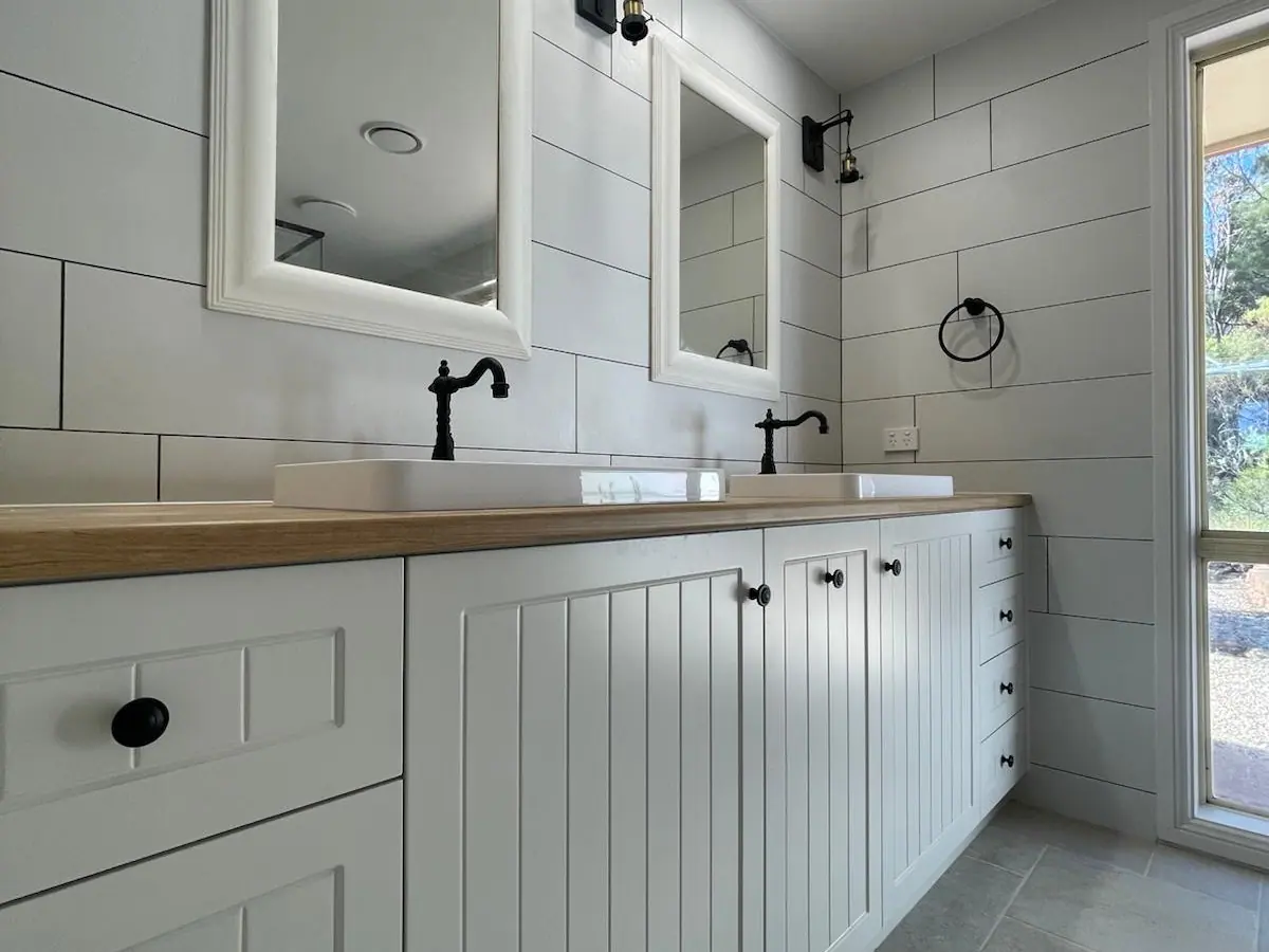Double vanity with white V-groove cabinet doors, black knobs and tapware, a wood-grain benchtop and white-framed mirrors, Amaroo home