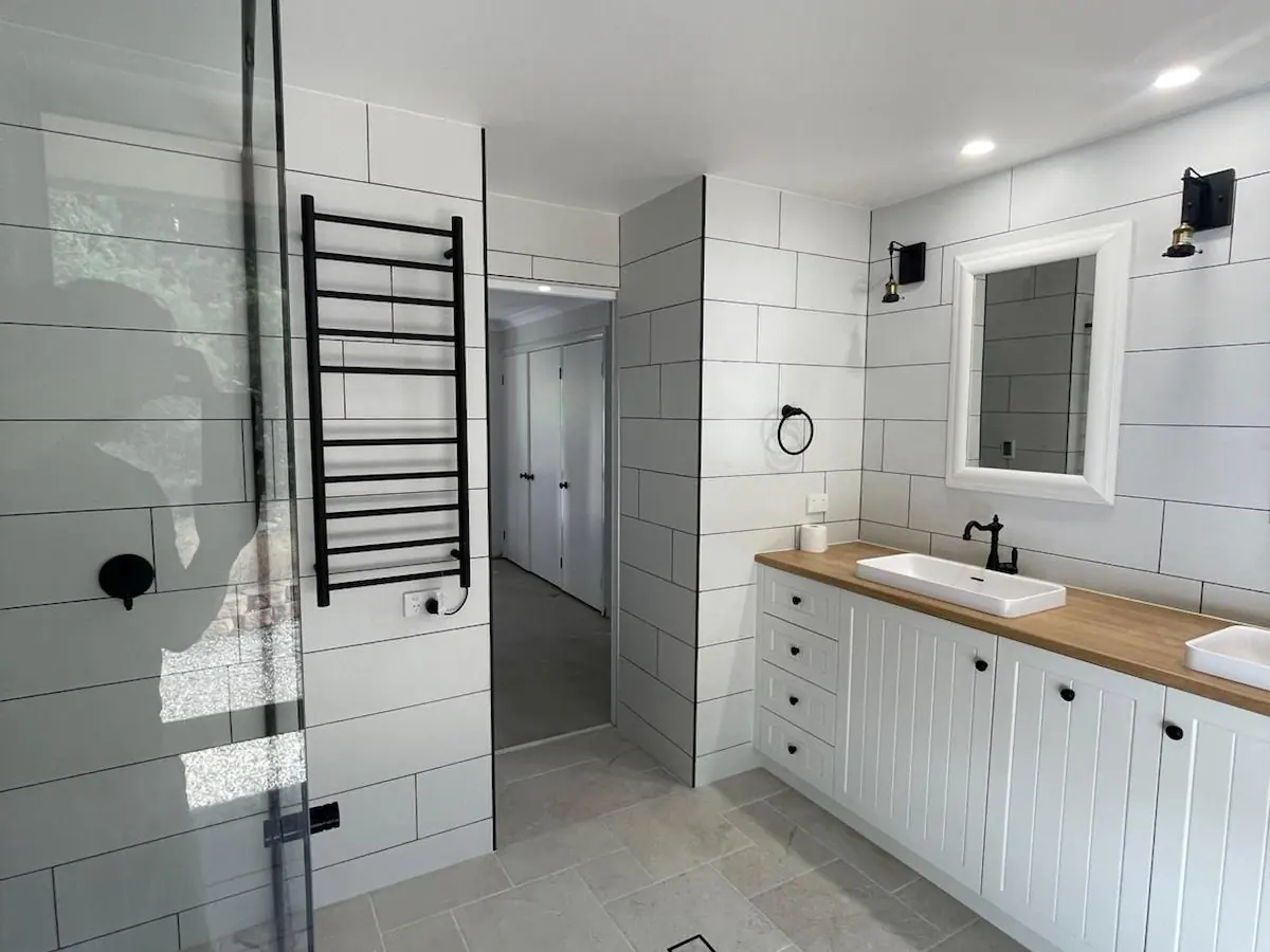 Main bathroom seen past a glass shower screen, with a black towel ladder, a white vanity and stone-look floor tiles, Amaroo home