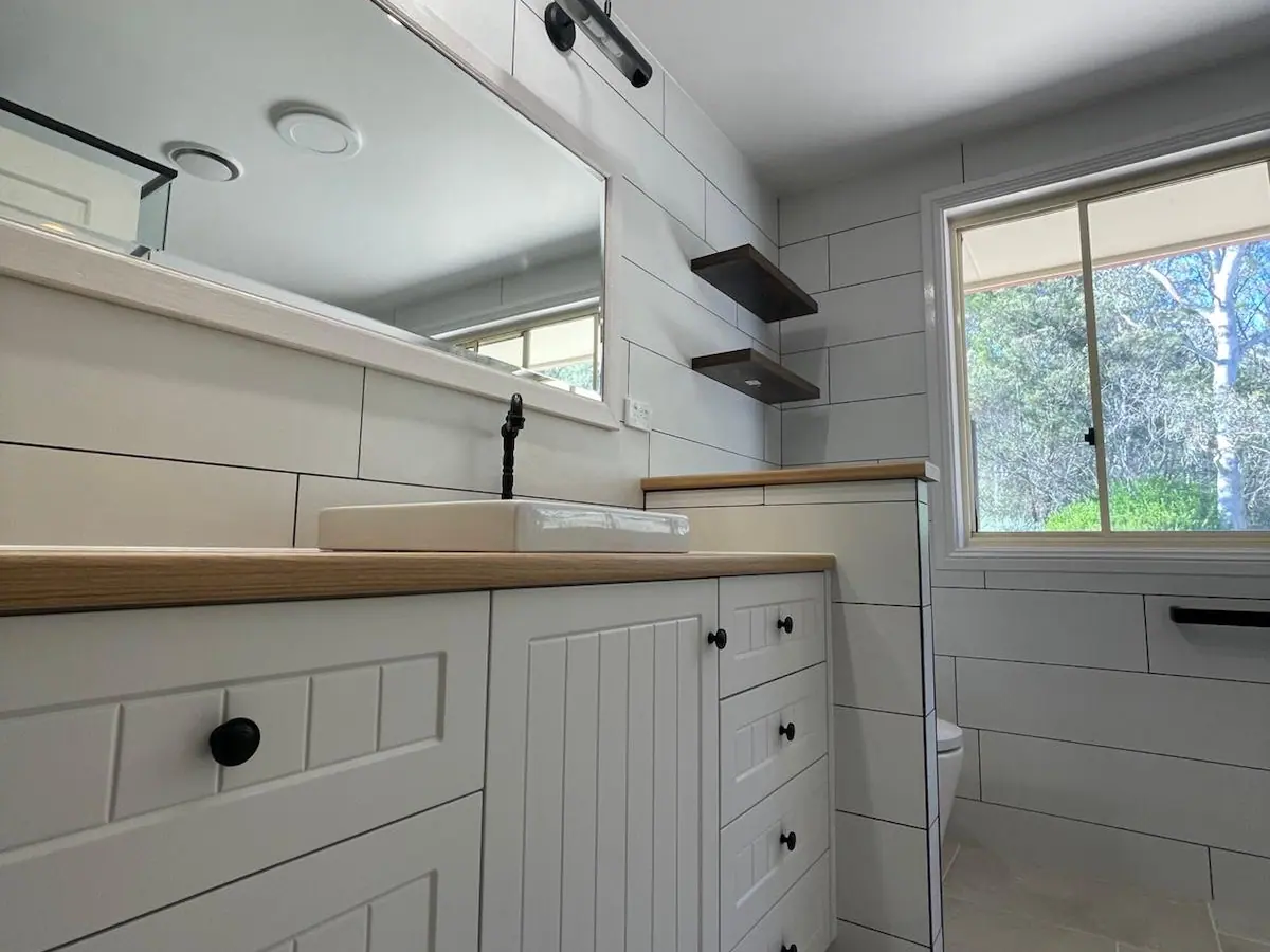 White V-groove vanity with a timber-look benchtop and inset basin, a long mirror, black wall lights and floating timber shelves, Amaroo home