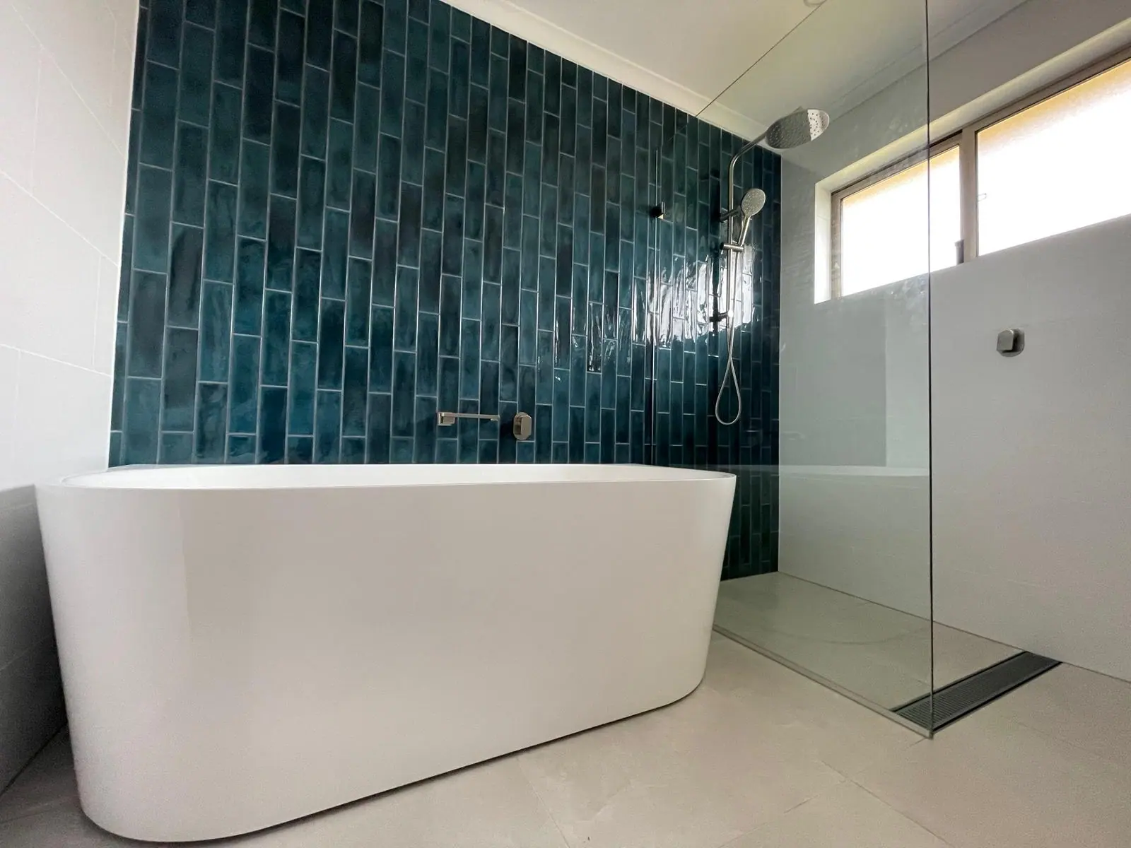 Freestanding bath in front of a wall of vertical teal gloss tiles, beside a frameless walk-in shower with a linear drain, Banks home
