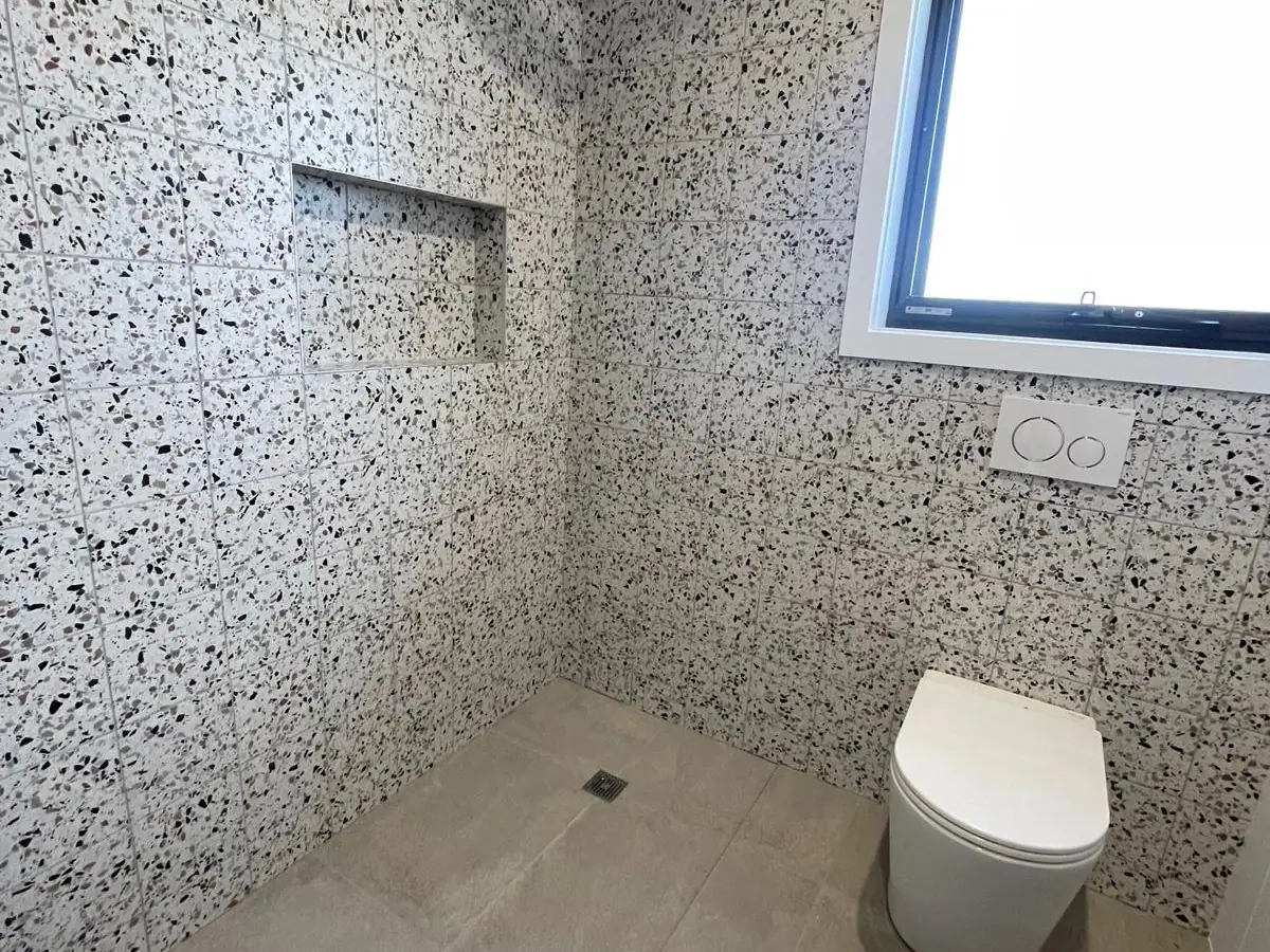 Open wet-room shower and toilet with speckled terrazzo-look wall tiles, a recessed niche and grey floor tiles, Casey home