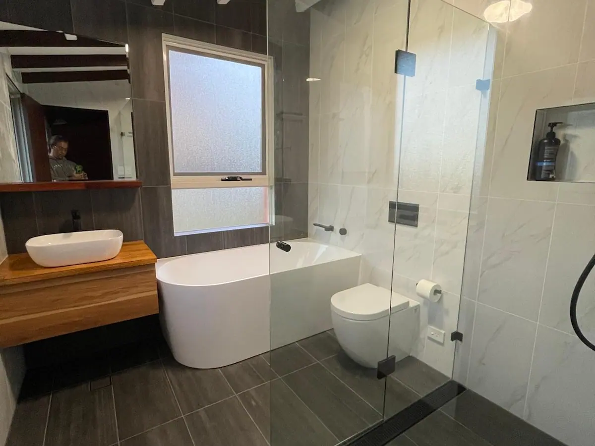 Bathroom with exposed ceiling beams, a back-to-wall bath under a frosted window, a frameless shower screen and a timber vanity with a vessel basin, Flynn home