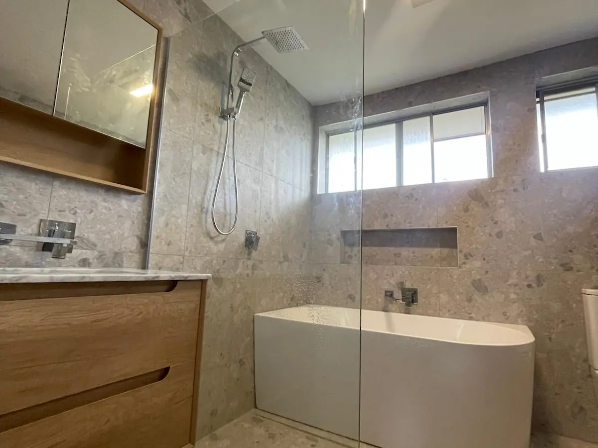 Bathroom in large terrazzo-look tiles with a back-to-wall bath, a frameless shower screen, a timber wall-hung vanity and a mirror cabinet, Richardson home