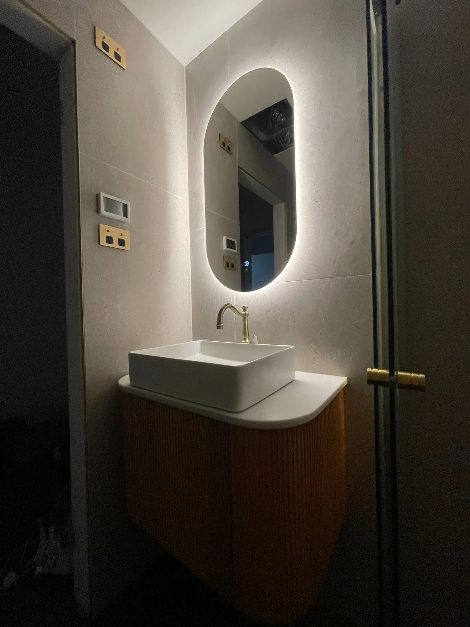 Floating fluted timber-look vanity under a backlit oval mirror, with brass tapware and brass switch plates, Wanniassa home